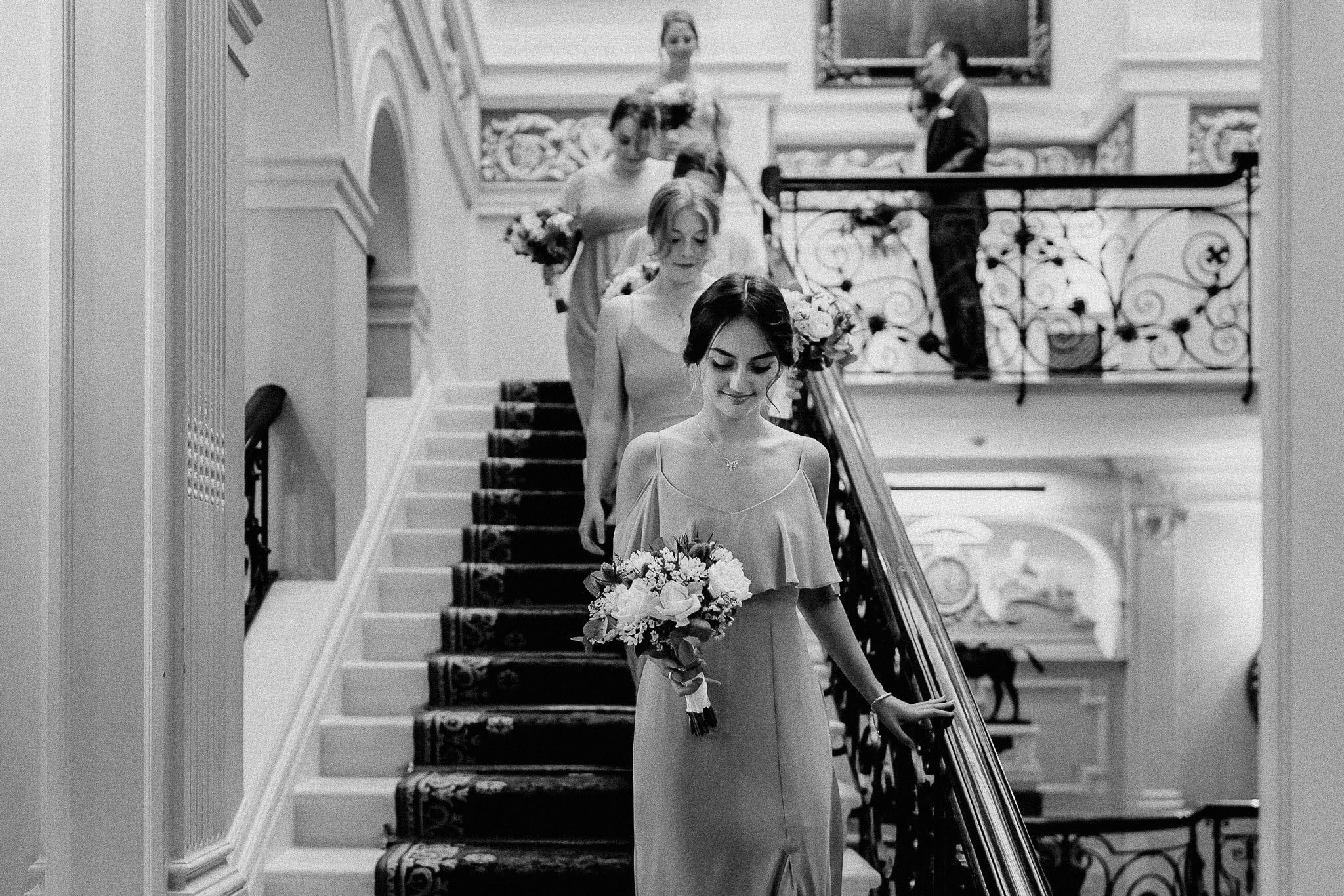 Wedding party ascending stairs with bridesmaids holding bouquets