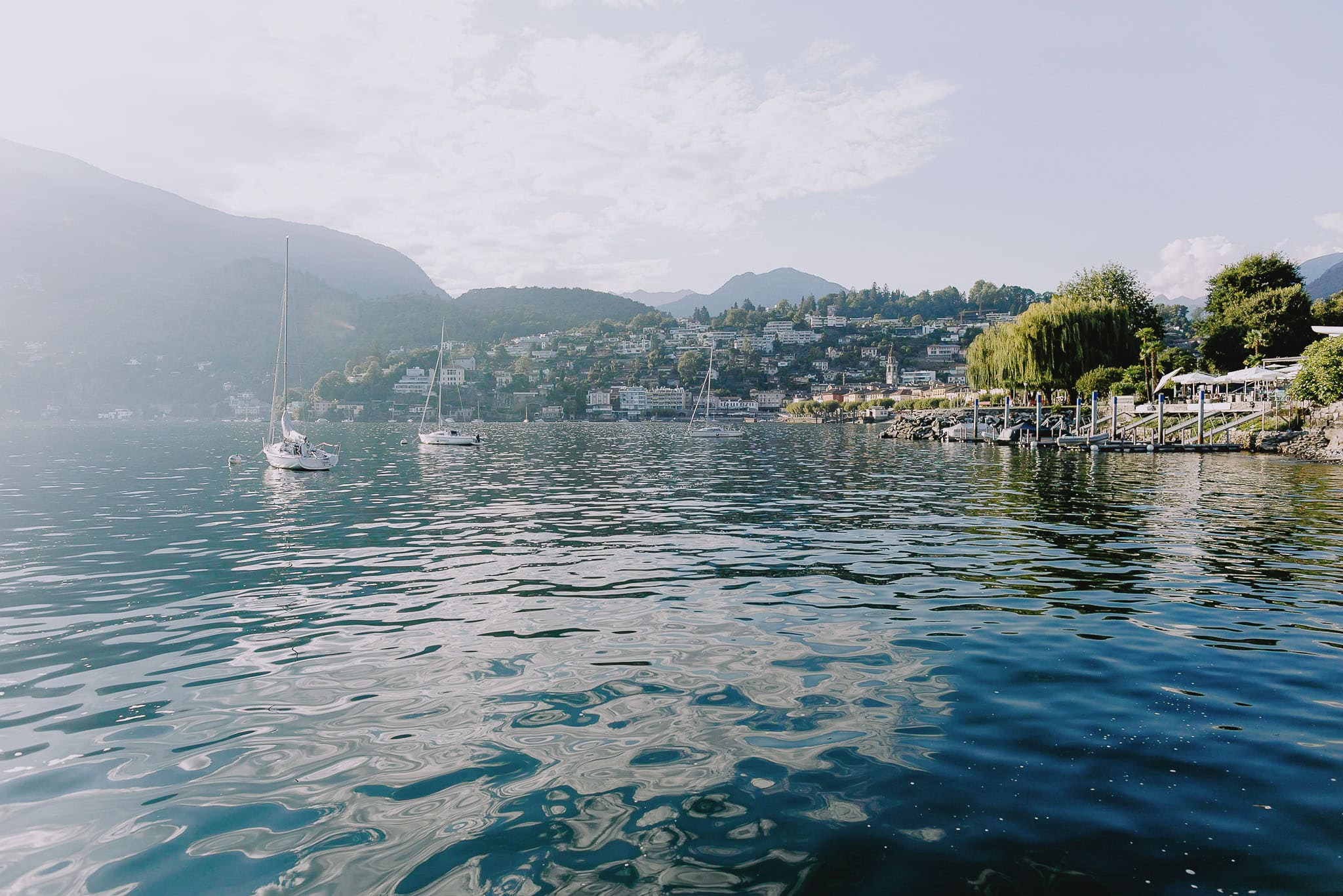 Sailboats on a lake with a town nestled in the hills, perfect for a destination wedding.